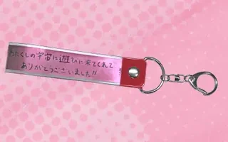 銀色のテープのキーホルダーの画像。テープに「わたくしの宇宙に遊びに来てくれて ありがとうございました!!」と手書きの文字があり、赤い留め具と金具が付いている。